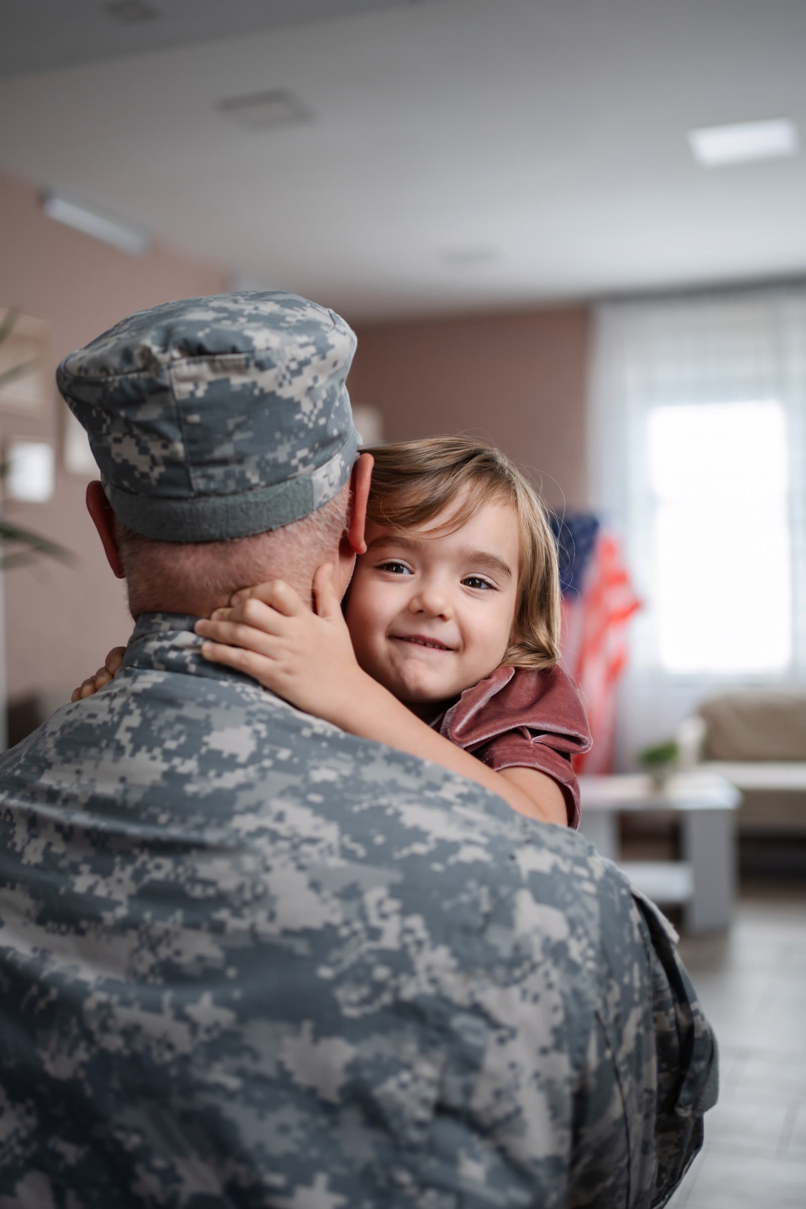 Smiling daughter in her soldier father's arms with the American flag behind them