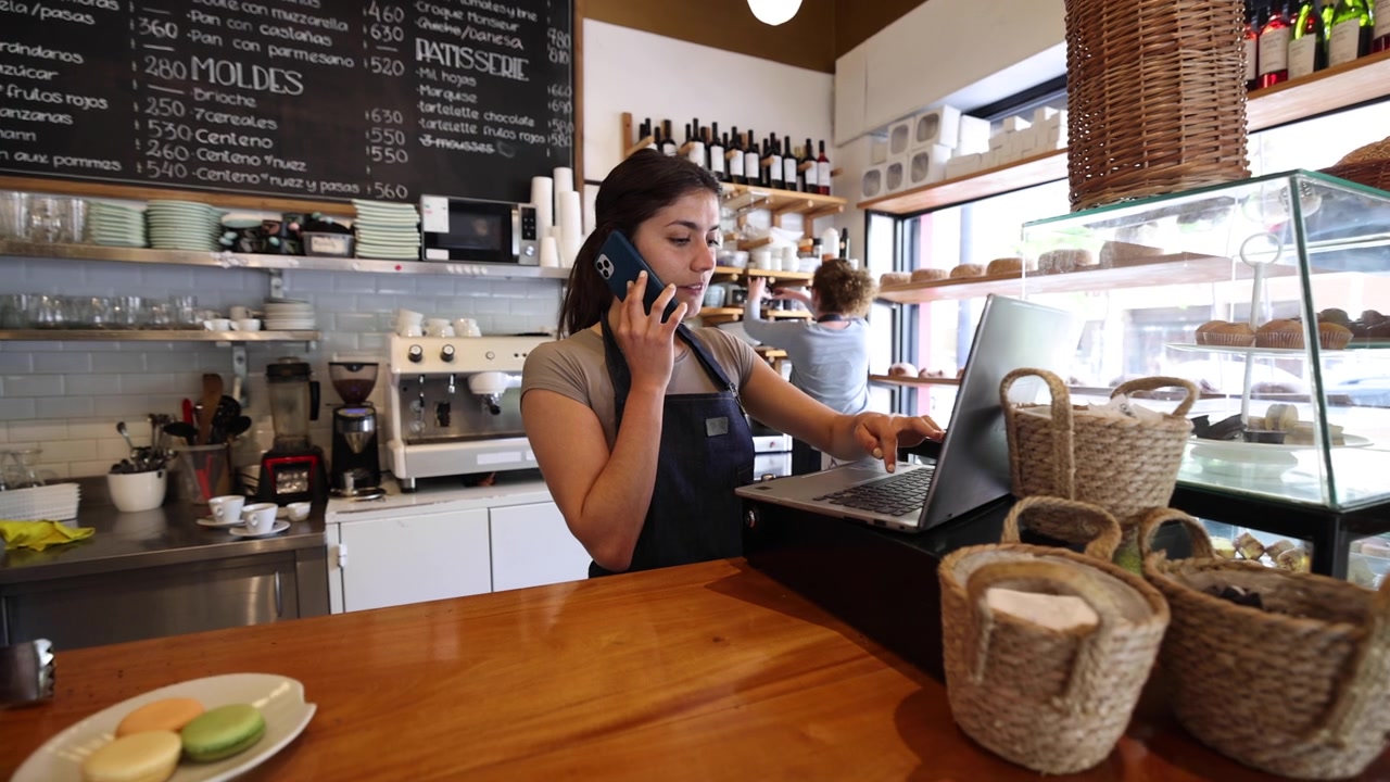 Cafe owner on the phone placing an order at her laptop behind the counter