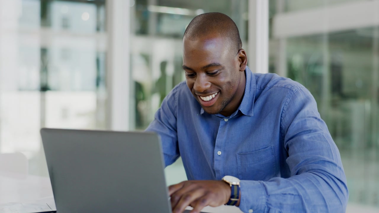 Smiling man working on a laptop in a bright office
