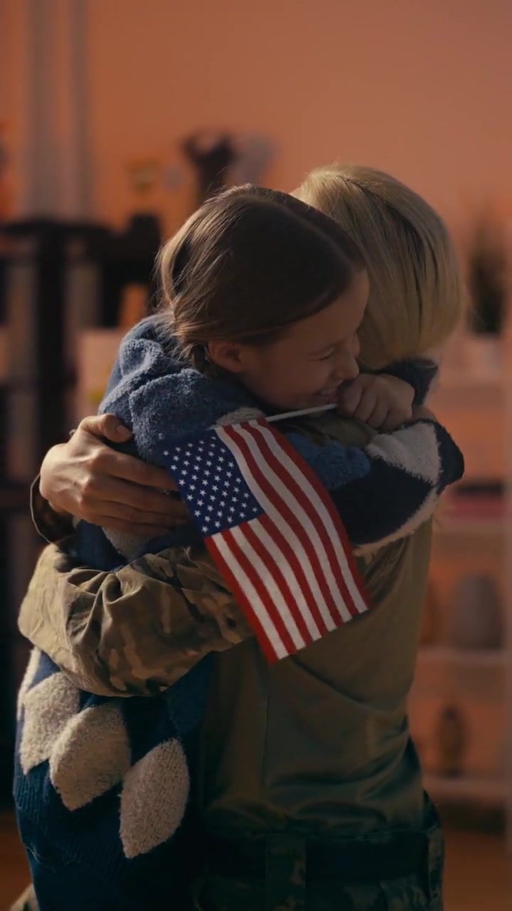 Daughter holding a small American flag hugging her soldier mother on homecoming day