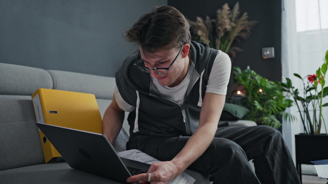 Young man reviewing paperwork on his laptop at home