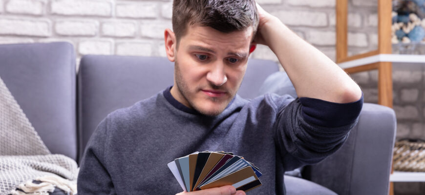 a man looking uncertain, head in hand, with his stack of credit cards wondering how many is too many credit cards to have