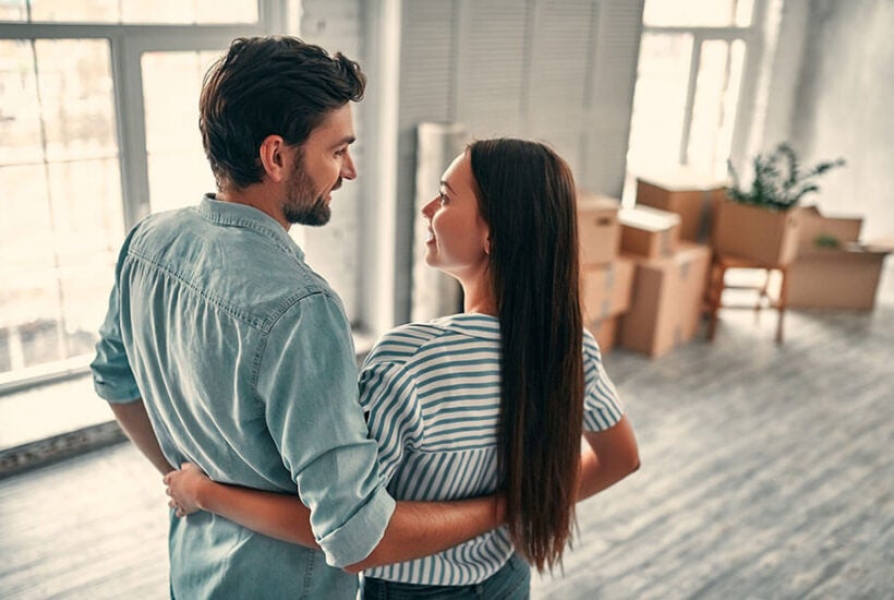 A happy young couple is taking a break from unpacking boxes in their new home bought with an adjustable-rate mortgage loan.