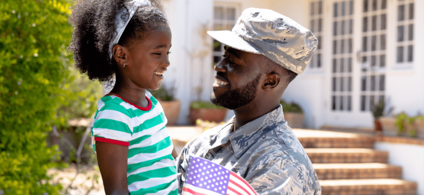 A military dad holding his young daughter outside of their home