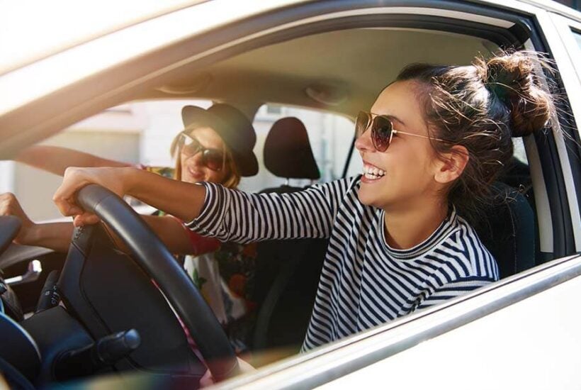 A young woman smiling as she drives her new car after saving for the down payment with her high-yield account.
