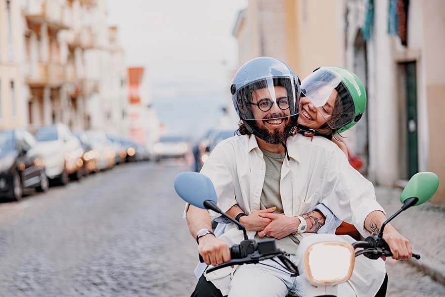 A happy 30-something couple driving a moped on a European vacation paid for by their high-yield savings account.