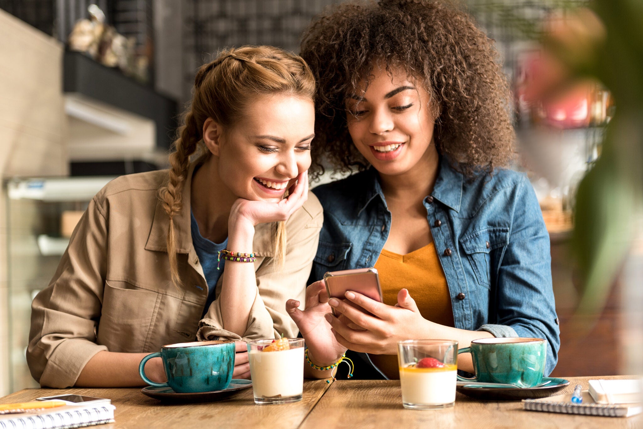 Two friends smiling while checking their phone as they sign up for America's Credit Union referral program.