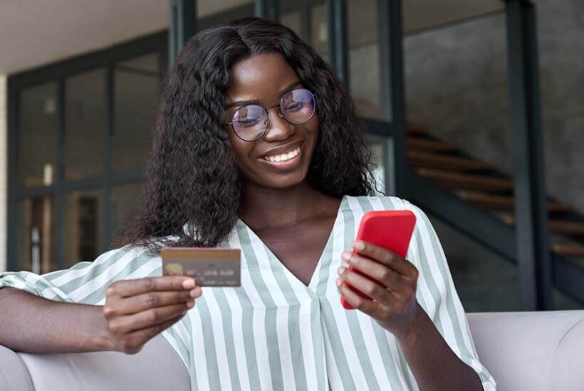 A woman is smiling while making purchases online with her America's Credit Union debit card.